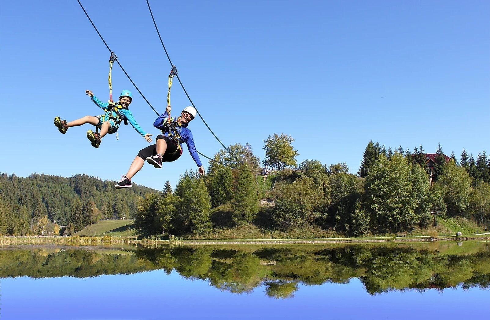 Dos personas hacen bungee jumping sobre un cuerpo de agua, con un área boscosa al fondo.