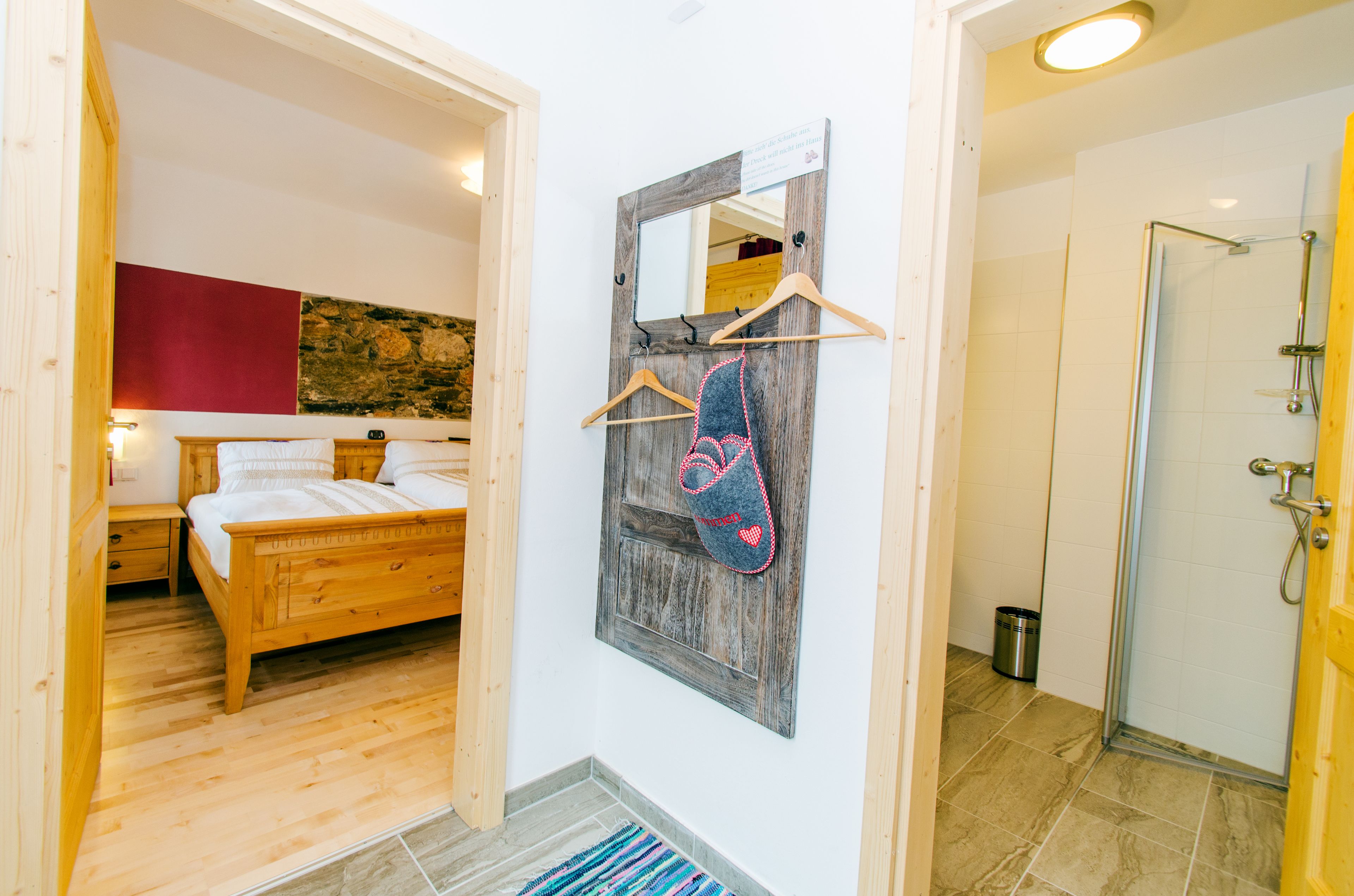 A bedroom with a wooden bed, a nightstand, a wall-mounted mirror, and a red abstract painting.