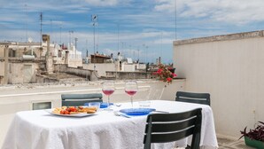 Una mesa para dos con mantel blanco, dos copas de vino tinto, un plato de comida y una planta en maceta.