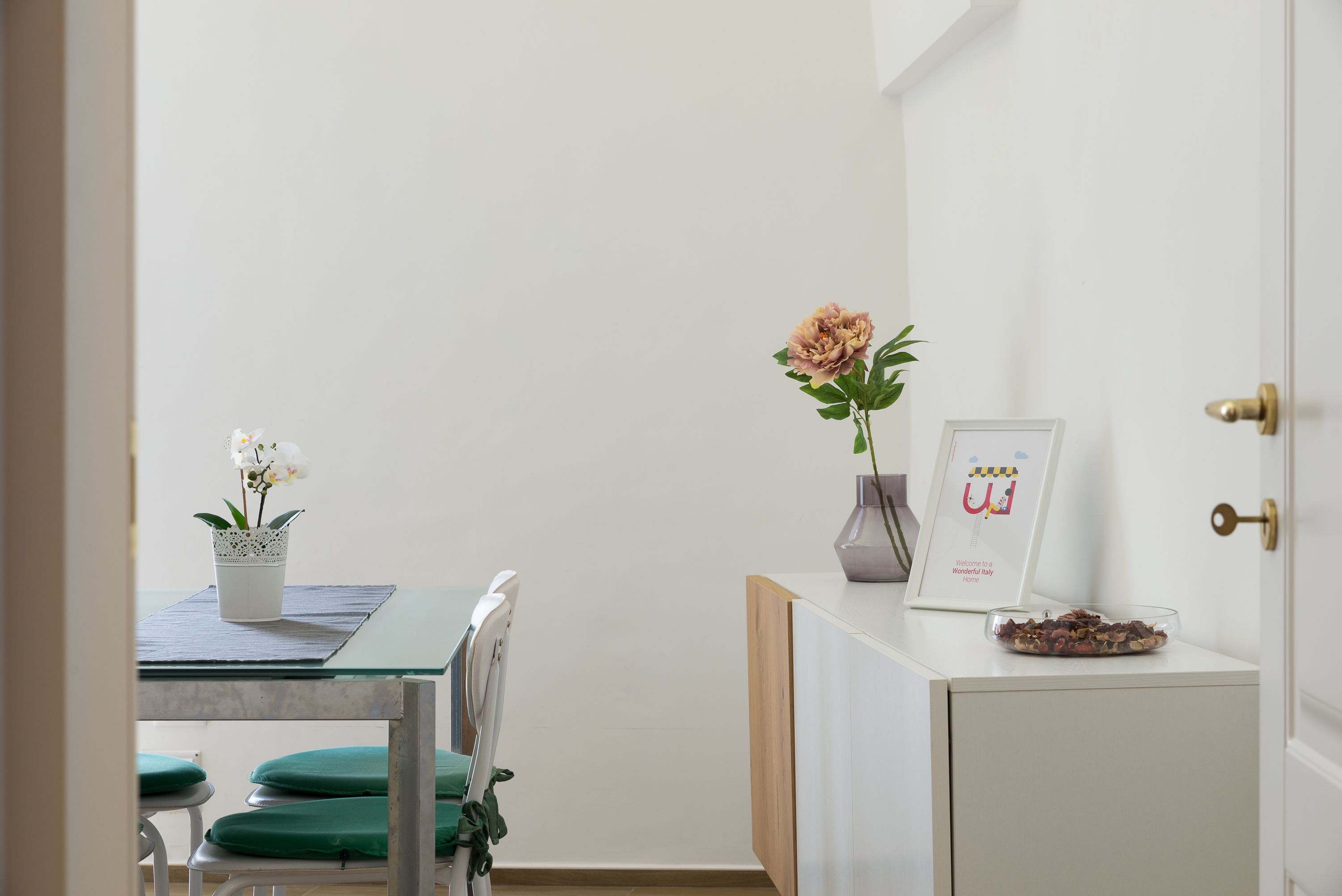 A dining area with a table, chairs, a vase with flowers, and a framed picture on a cabinet.