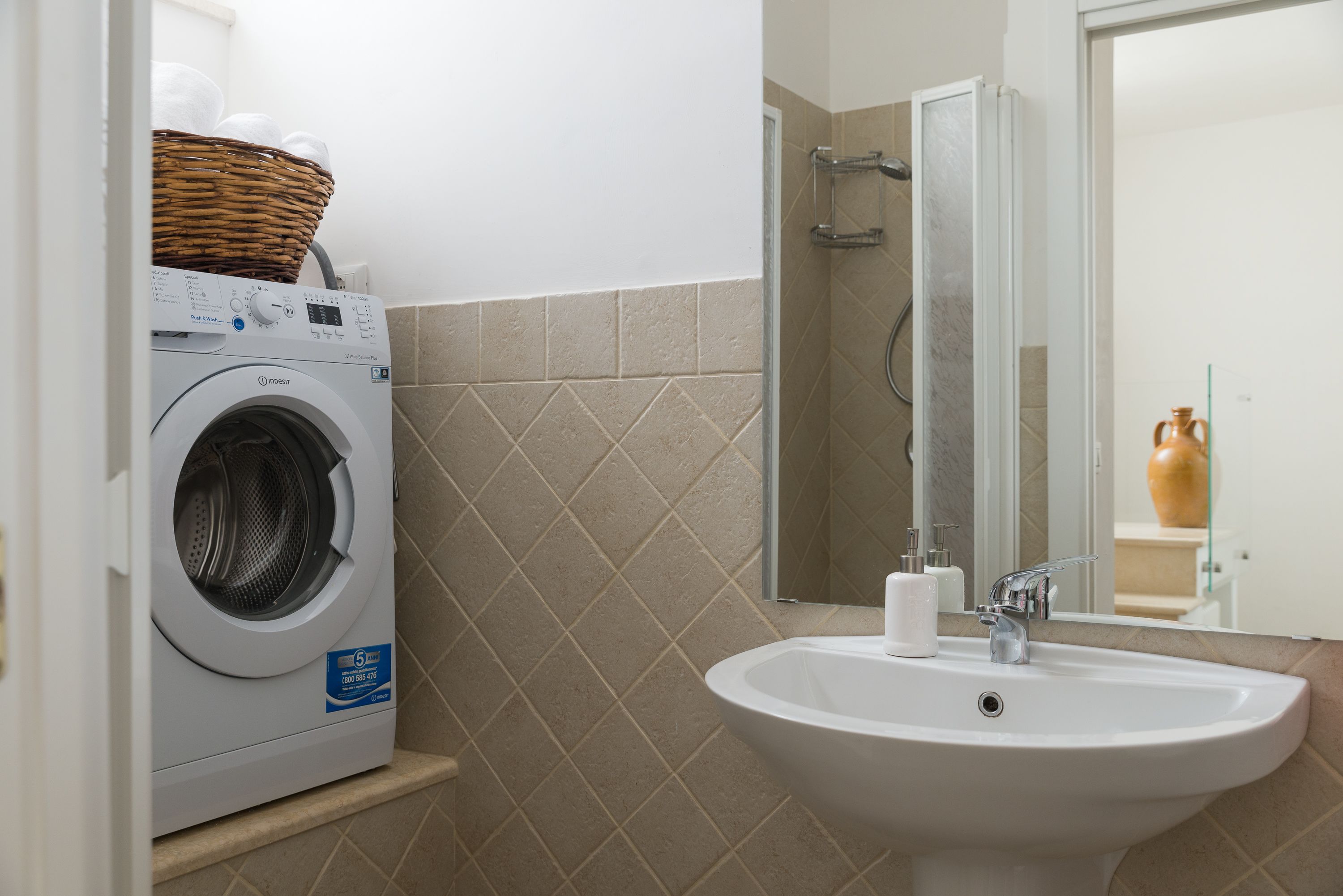 Une petite salle de bain équipée d’un lave-linge, d’un lavabo et d’un miroir.