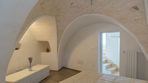 Un dormitorio con una cama grande, un tocador con un florero y una escalera que lleva a un piso superior.