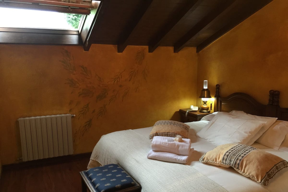 A bedroom with a bed, a nightstand, a lamp, a window, and a radiator.