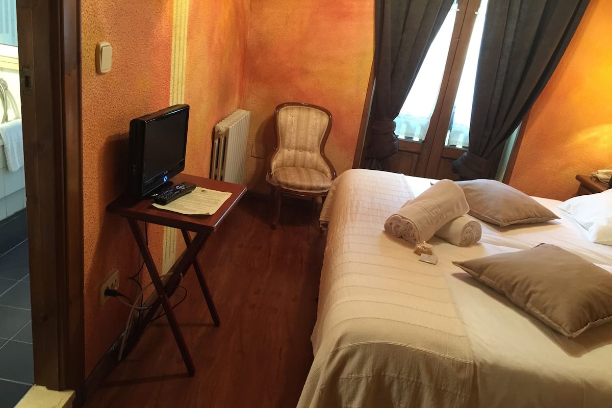 A hotel room with a bed, a chair, a desk with a computer and paperwork, and a radiator.