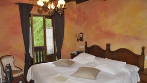 A hotel room with a large bed, a chair, a nightstand, and a window with curtains.