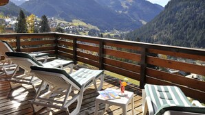 A wooden deck with lounge chairs and a table, overlooking a mountainous landscape. - Hôtel les Triolets (Chatel)