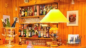 A wooden bar area with stools, a bar counter, and shelves stocked with bottles and glasses. - Hôtel les Triolets (Chatel)