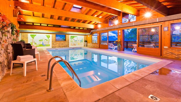 An indoor swimming pool with wooden beams, lounge chairs, and a view of the outdoors. - Hôtel les Triolets (Chatel)