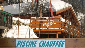 A wooden cabin with a sign reading "PISCINE CHAUFFÉ" and a snowy landscape in the background. - Hôtel les Triolets (Chatel)