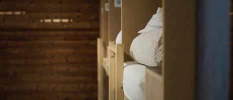 Filas de literas de madera en una habitación con techo inclinado y paredes de madera. Cada cama tiene un número en la pared superior.