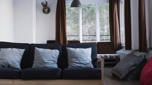 A modern living room with a dark blue sofa, two light grey cushions, a wooden coffee table, and a hanging pendant light. - 1861 Châtel Hostel (Chatel)