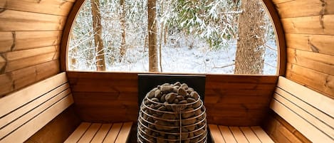 A wooden sauna with a circular window, a wooden bench, and a stone structure in the center.