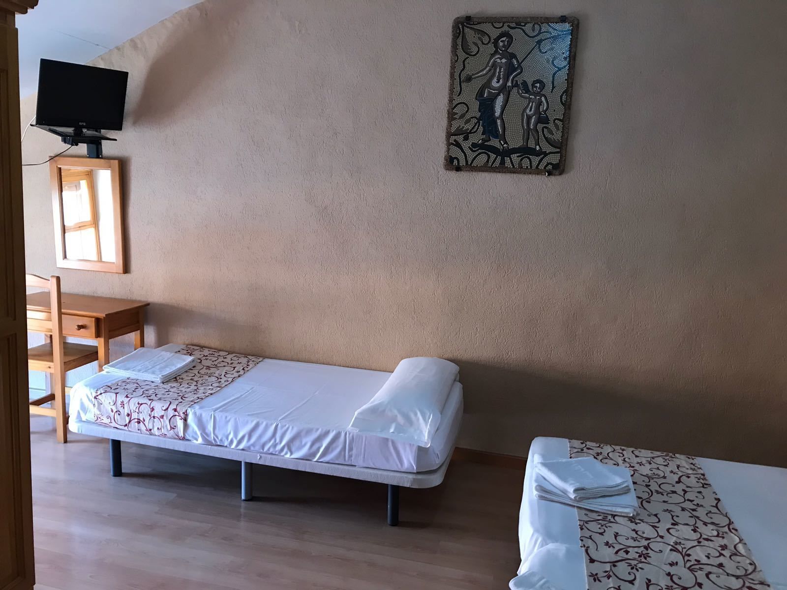 Una habitación con dos camas individuales, un escritorio, una silla, un televisor y un cuadro en la pared.
