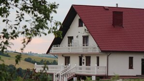 A two-story white building with a red roof, a balcony, and a staircase leading to the entrance. - Grand Panorama (Wisniowa)
