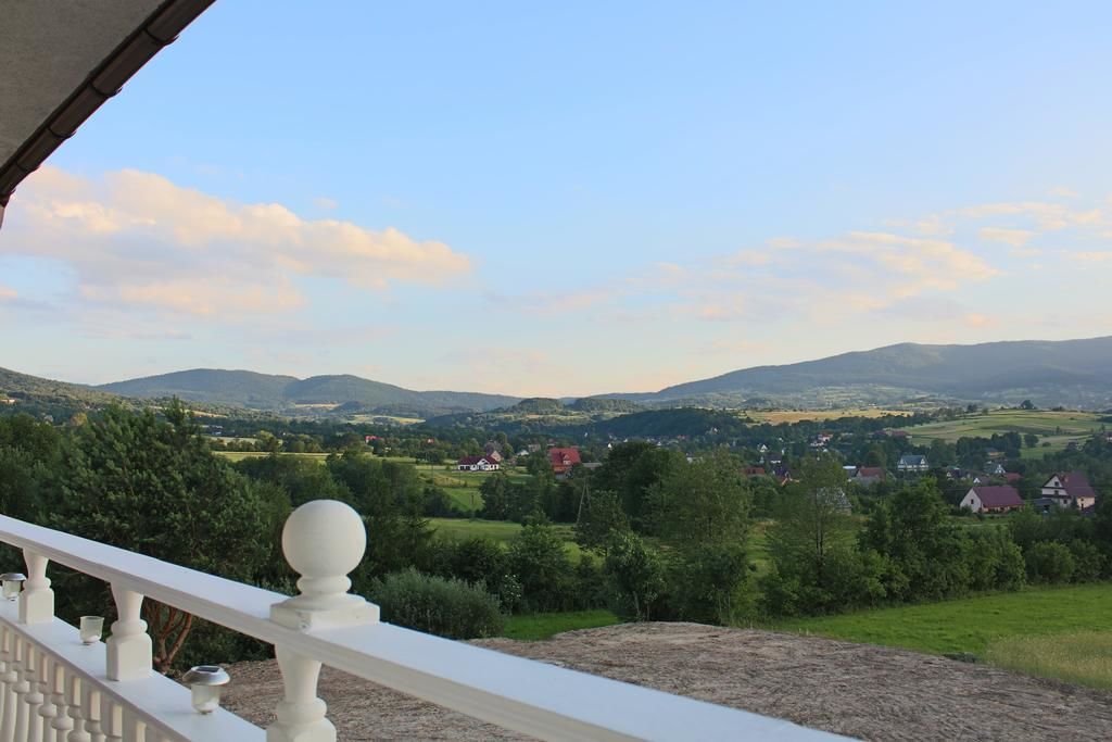 A balcony with a white balustrade overlooking a rural landscape with houses and hills.