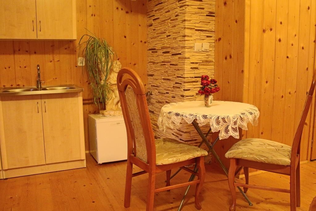 A small kitchen with wooden cabinets, a sink, a stove, and a table with a lace tablecloth and a vase of flowers.
