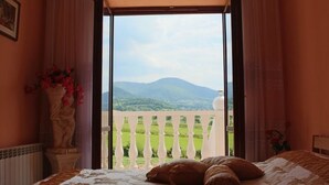 A bedroom with a bed, a statue, and a view of green fields and mountains through an open balcony door. - Grand Panorama (Wisniowa)