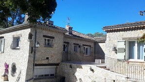Un edificio de piedra con un balcón, una ventana pequeña con reja metálica y una puerta con ventanal.