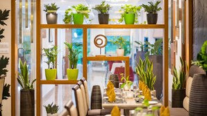 Un interior de restaurante con un separador de madera, varias plantas en macetas y un área de comedor con sillas y mesas.