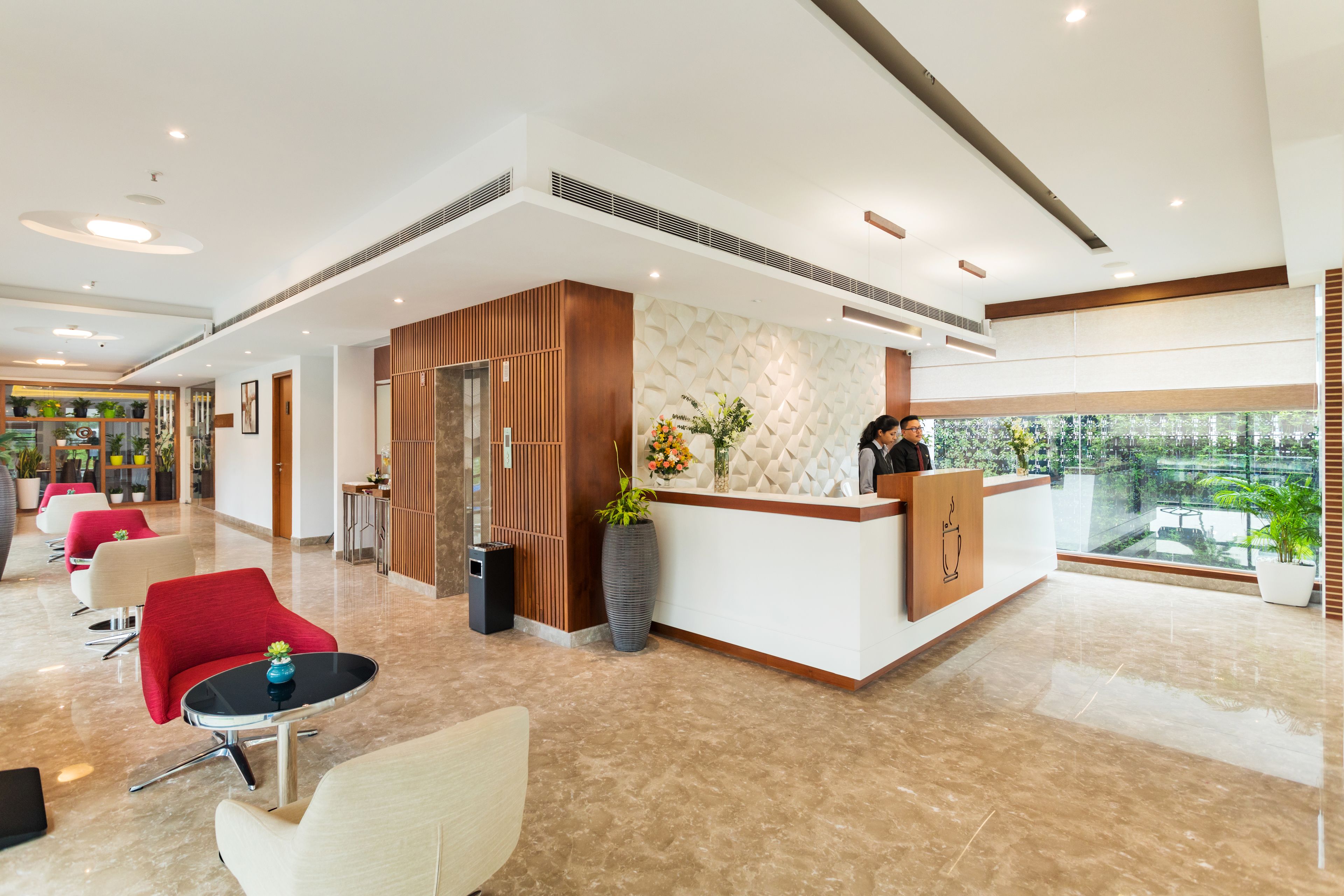 A modern hotel lobby with a reception desk, seating area, and a view of the outdoors.