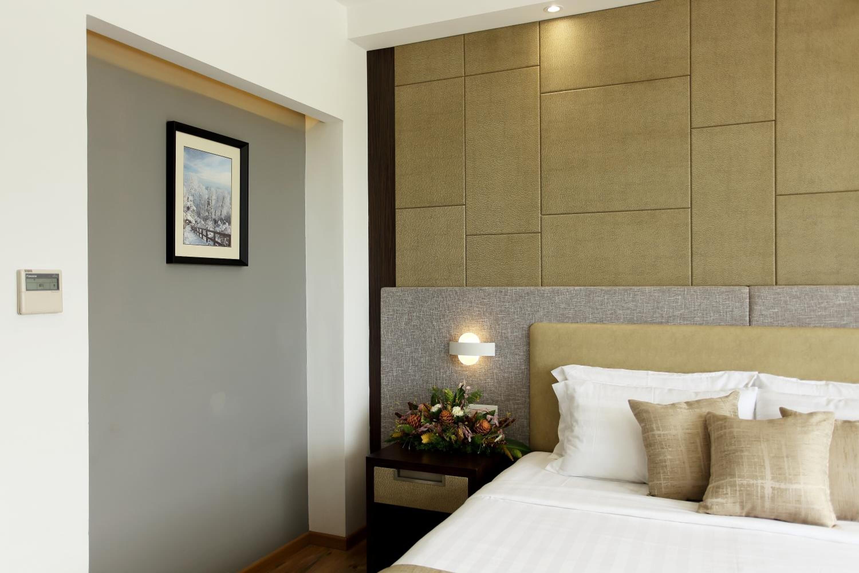 A hotel room with a bed, a nightstand with a flower arrangement, and a framed picture on the wall.