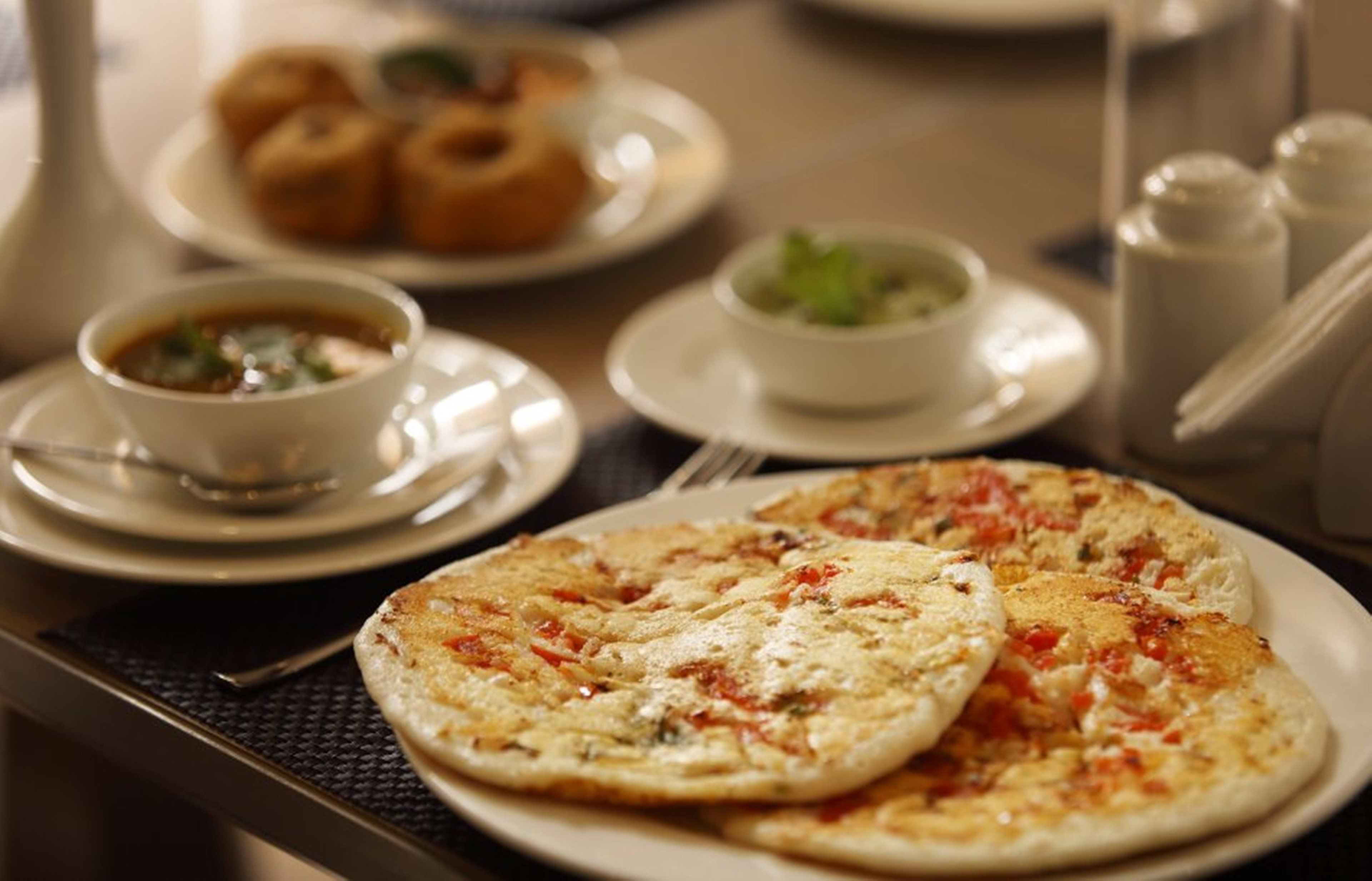 A dining table with a plate of pizza, a bowl of soup, and a plate of pastries.