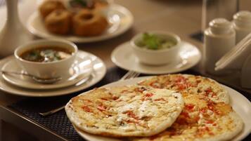 A dining table with a plate of pizza, a bowl of soup, and a plate of pastries.