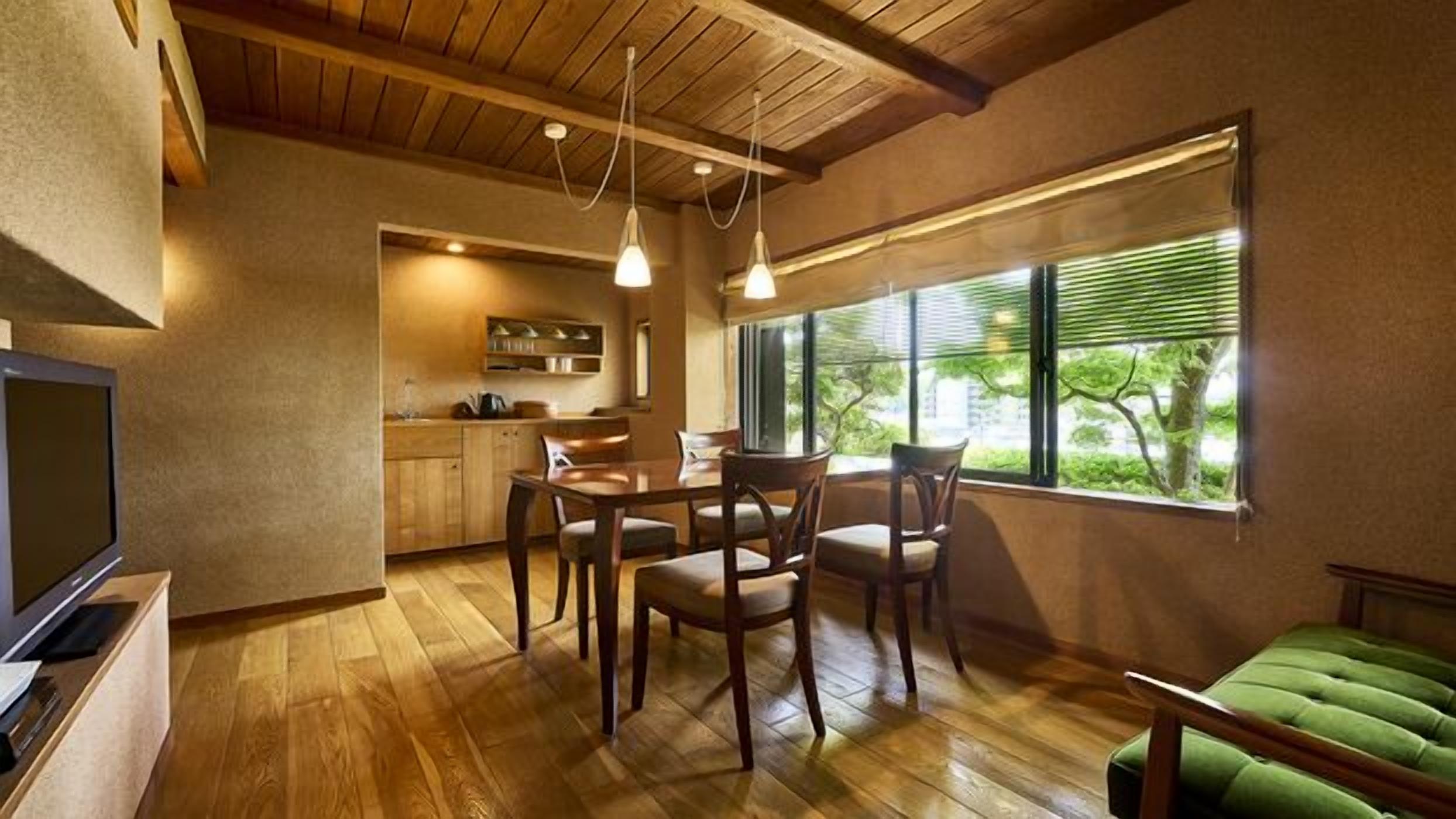 Una sala de estar acogedora con piso de madera, un sofá verde, un comedor con mesa y sillas, y una cocina al fondo.