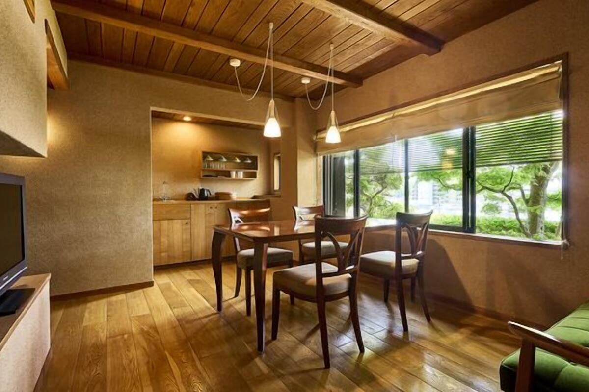 Uma sala de estar acolhedora com piso de madeira, um sofá verde, uma área de jantar com mesa e cadeiras, e uma cozinha ao fundo.