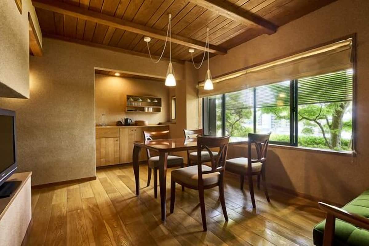 Una sala de estar acogedora con piso de madera, un sofá verde, un comedor con mesa y sillas, y una cocina al fondo.