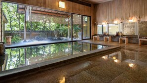 Un spa moderno con una zona de aguas termales de cristal, paneles de madera y una barra de piedra con lavamanos y espejos.