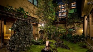 Un patio con una formación rocosa, un pequeño árbol y un farol japonés tradicional.
