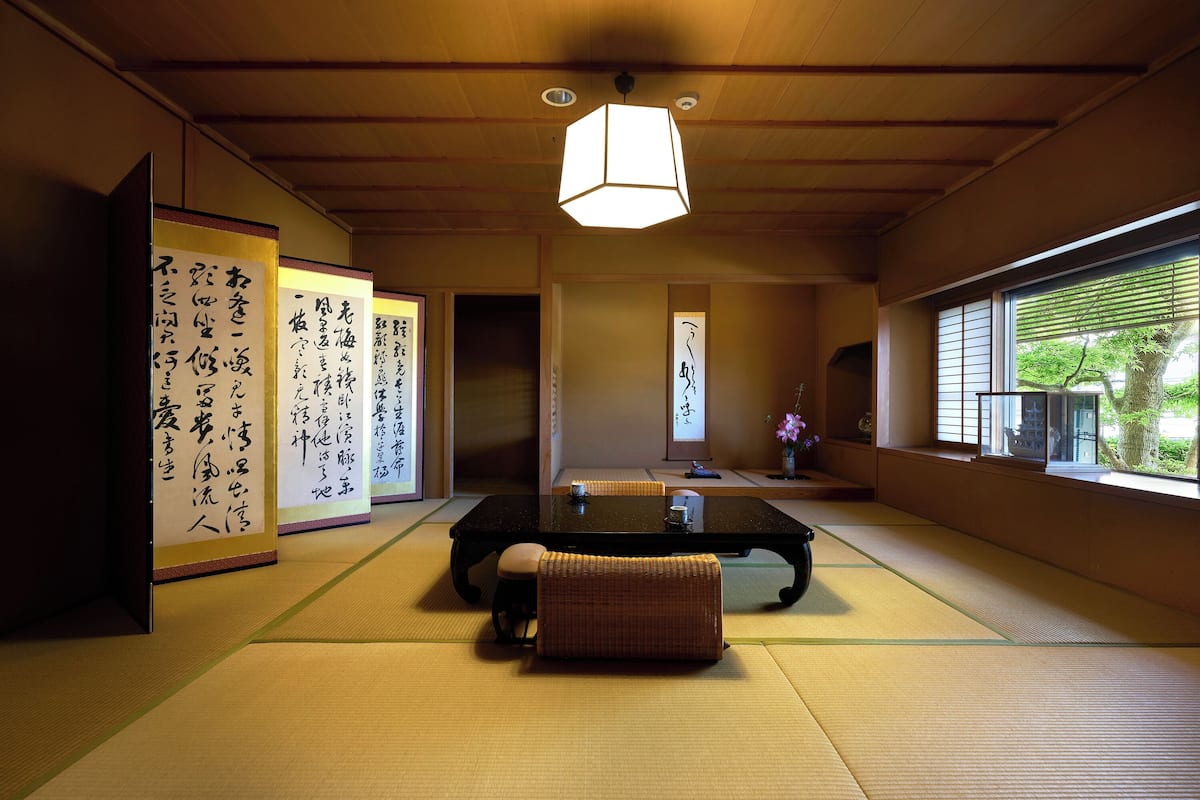Um quarto japonês tradicional com tatames, uma mesa baixa e rolos de caligrafia.