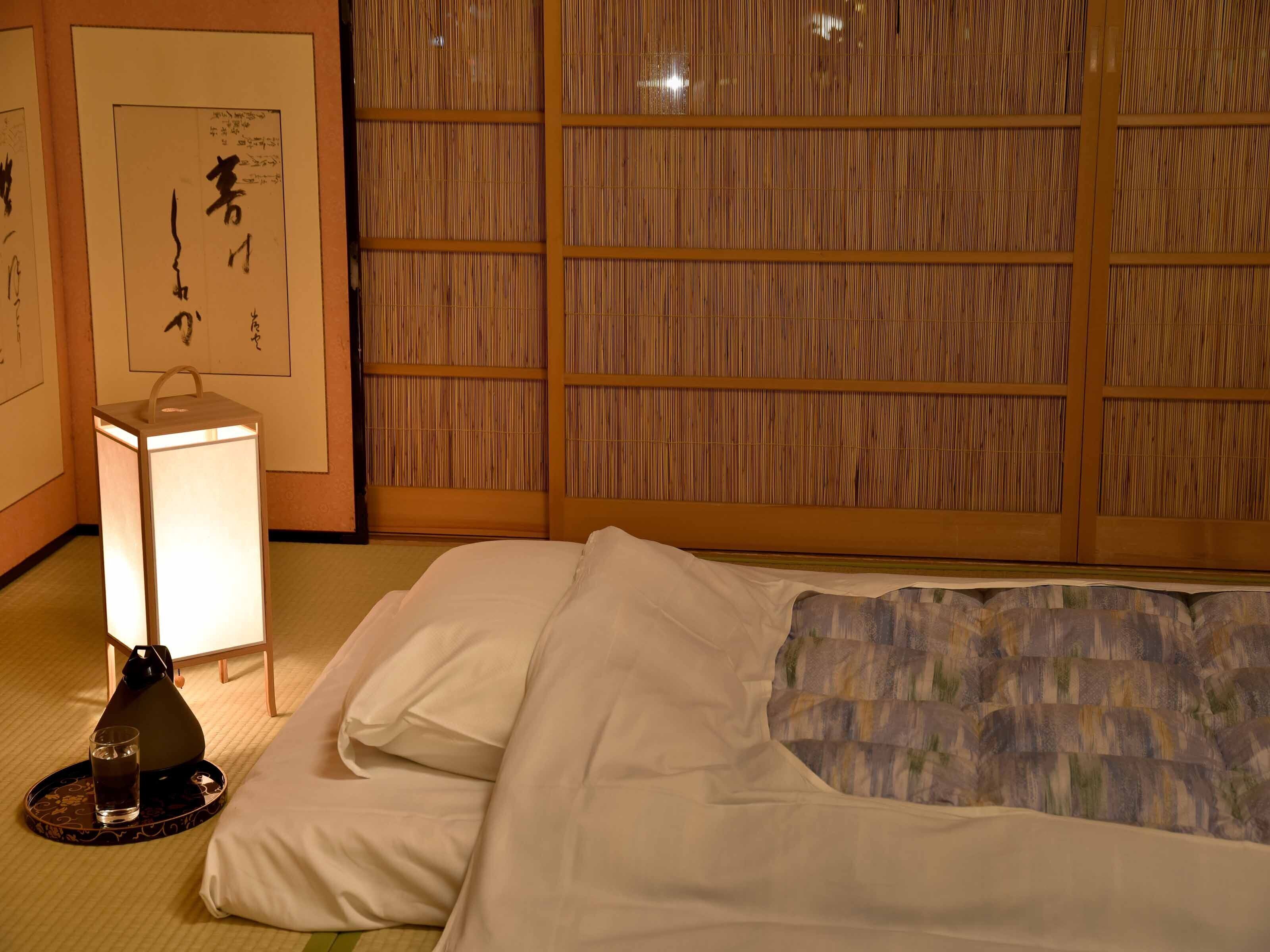 A hotel room with a bed, a bedside table with a lamp, and a wall with a traditional Japanese shoji screen.