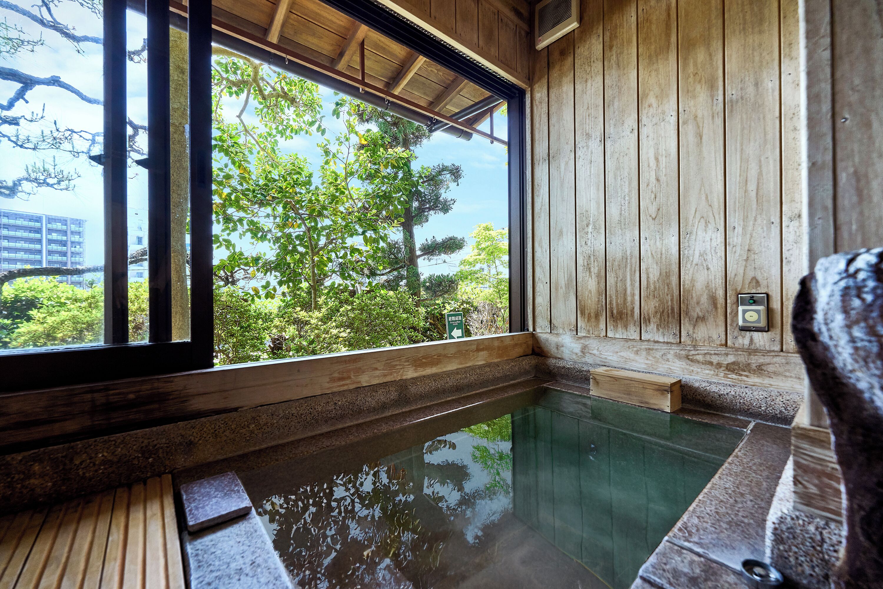 A traditional wooden bath with a clear view of trees and buildings outside.