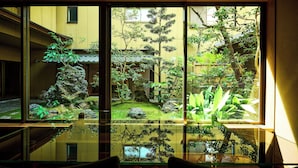 Habitación con un ventanal que ofrece vistas a un jardín japonés tradicional con rocas, plantas y un pequeño estanque.