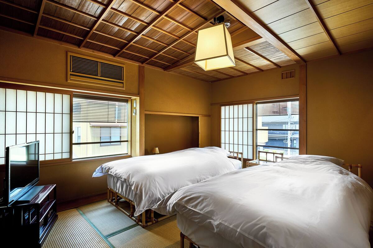 Quarto de hotel com duas camas, televisão e janelas amplas com persianas.