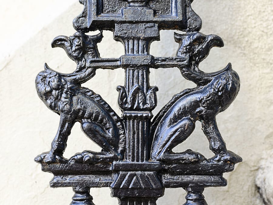 A close-up of a decorative metal gate with intricate designs, including two animal figures and a central column.