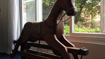 A wooden rocking horse in a room with large windows and a blue carpet.