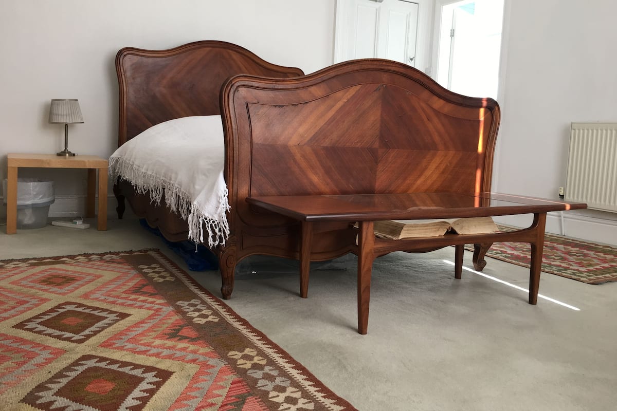 A bedroom with a wooden bed, a nightstand, a lamp, and a patterned rug.
