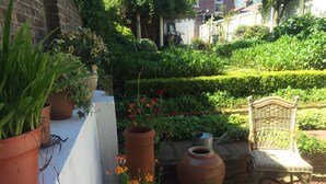 Un jardín con plantas en macetas, una silla de mimbre y una maceta de terracota grande.