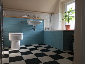 A bathroom with a white toilet, a sink, and a shower. The walls are painted teal, and the floor has a black and white checkered pattern. - Square Tree House (Liverpool)