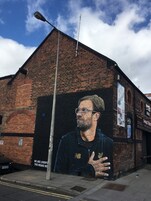 A mural of a man on a brick building with a street lamp in front.
