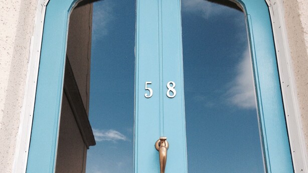 Una puerta turquesa con el número 58, un aldabón de bronce y una ranura para el correo.