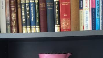 Una estantería con varios libros y una jarra rosa con estampado de cuadros.