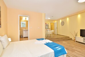 Habitación de hotel con cama, escritorio, silla, televisor y baño visible a través de una puerta abierta.
