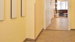 A hallway with a wooden floor, a white door, and a living area with a sofa and a lamp. - Central Studio 2 (Burgas)