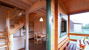Interior de una cabaña de madera con escalera, comedor y vistas al exterior.