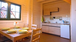 Un interior de madera con una mesa de comedor preparada para cuatro personas, una cocina con armarios de madera y un lavavajillas blanco.