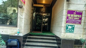 A hotel entrance with a staircase leading to a green carpeted area. There is a sign for 'The Metropolis Guest House' and an 'Assembly Station' sign. - The Metropolis Guest House Near RK Ashram Metro Station (New Delhi)